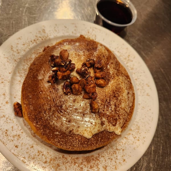 A Kountry Folks Homestyle Restaurant pancake with icing, cinnamon, and walnuts, with syrup on the side.