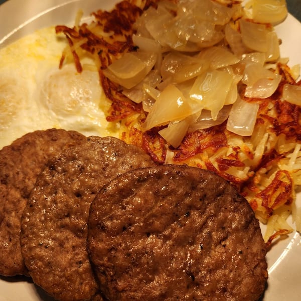 A Kountry Folks Homestyle breakfast with sausage patties, fried eggs, hash browns, and onions.