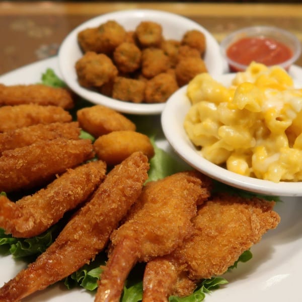Fried shrimp, hush puppies, fried okra, and macaroni and cheese on a white plate.