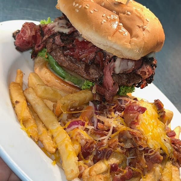 A Kountry Folks Homestyle Restaurant burger with fries topped with cheese, bacon, and red onions.